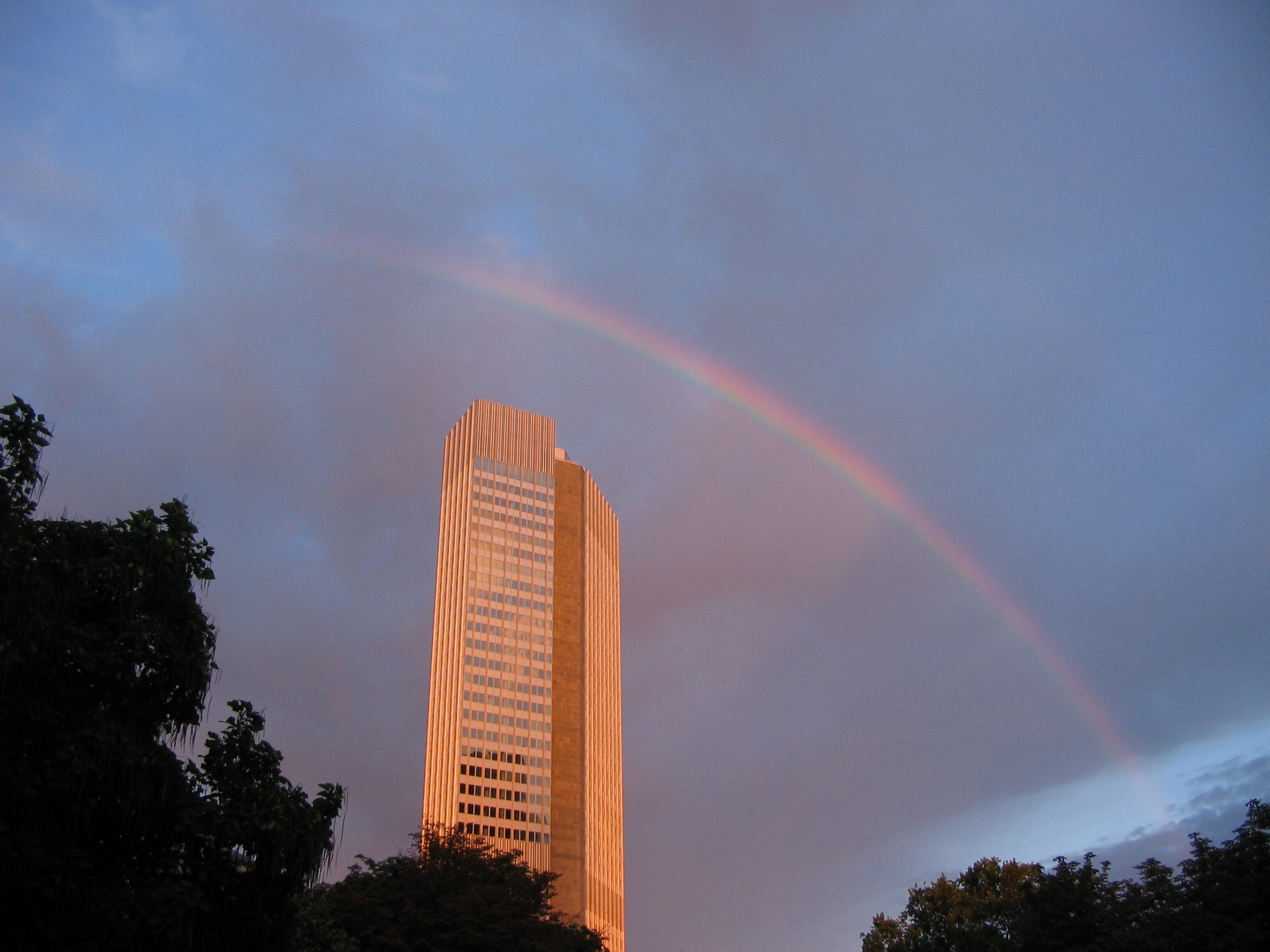 The Eurotower in Frankfurt, the historic seat of the European Central Bank, under a rainbow at dusk.