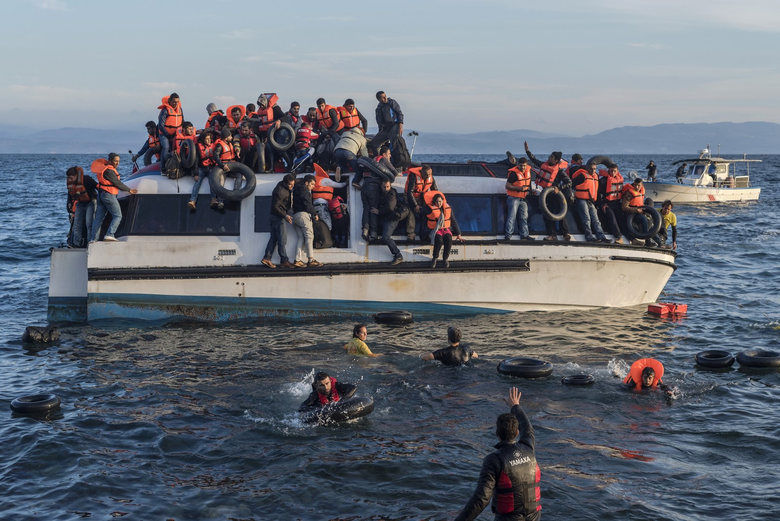 Bateaux de migrants et ferry sur la mer Égée au large de Lesbos au crépuscule, près de la route des passeurs depuis la Turquie