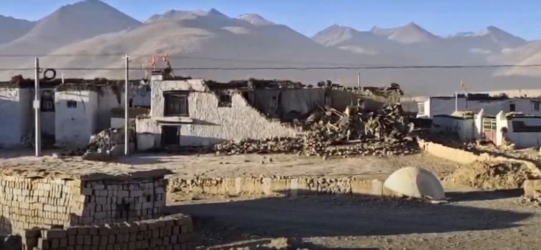 Earthquake-damaged homes in a high-altitude Tibetan village, rubble strewn across the plateau
